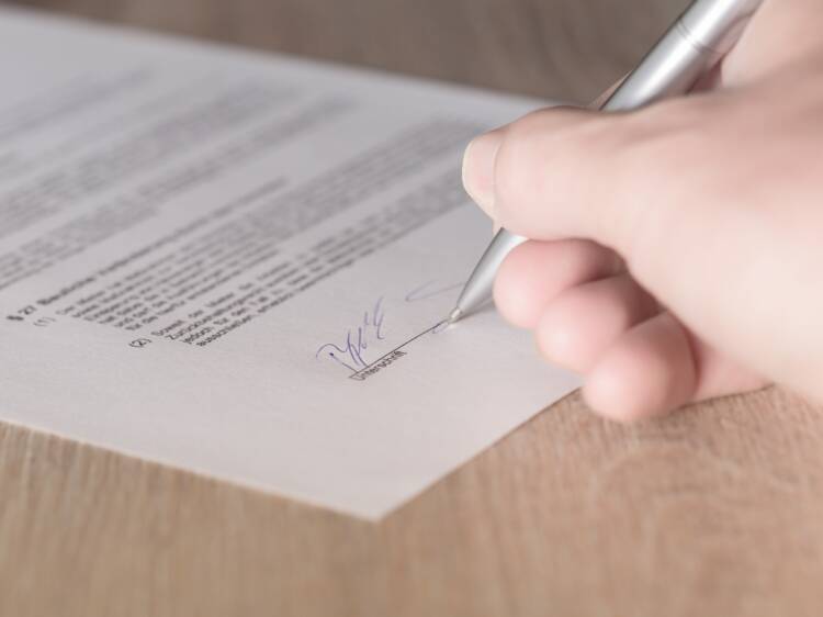 Sopimuspaperi ja kynää pitelevä käsi, joka on allekirjoittamassa.