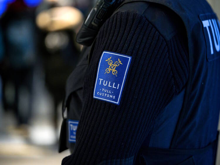 Tullitarkastaja Kittilän lentokentällä kuvattuna niin, että työasusta näkyy selkäosa ja hiha, jossa on Tullin logo.