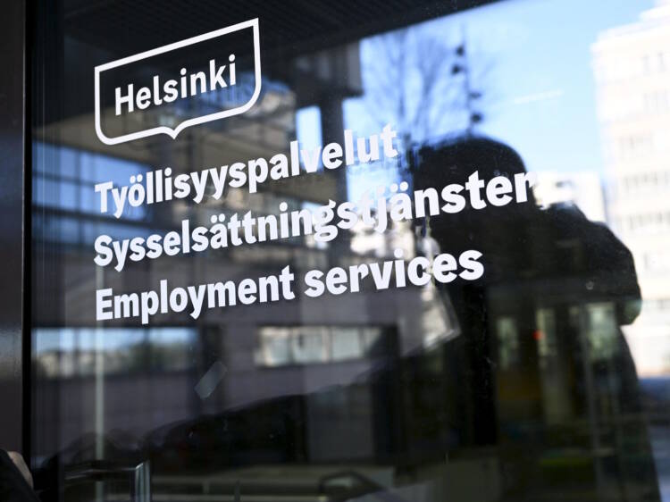 Ihminen avaamassa Pasilan TE-toimiston ovea, jossa on tekstiä kolmella kielellä.
