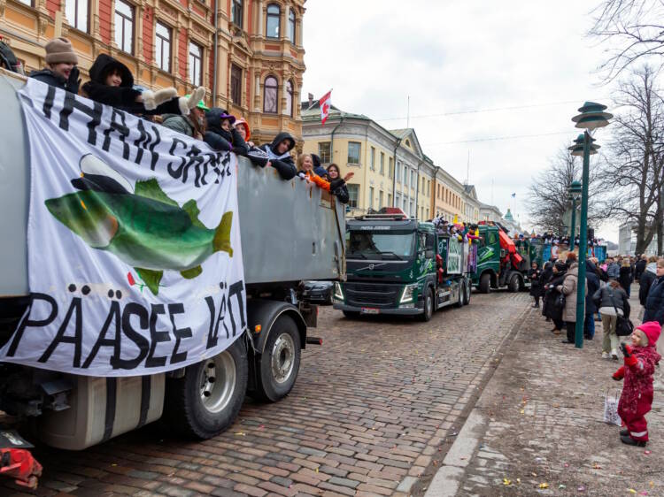 Abit matkustavat penkkariasuihin pukeutuneina kuorma-autojen lavoilla. Ihmisiä on kerääntynyt seuraamaan ajelua.