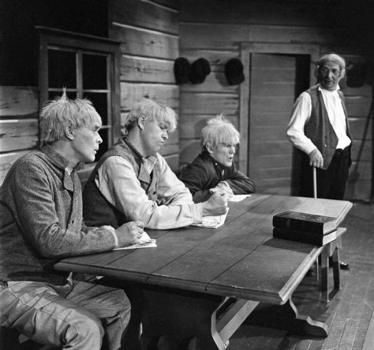 Kohtaus Aleksis Kiven näytelmästä Seitsemän veljestä. Lukkari yrittää opettaa Juhania, Tuomasta ja Lauria lukemaan. Kuva: Eero Suikki, 1967. Kouvolan kaupunginmuseo. CC BY 4.0.