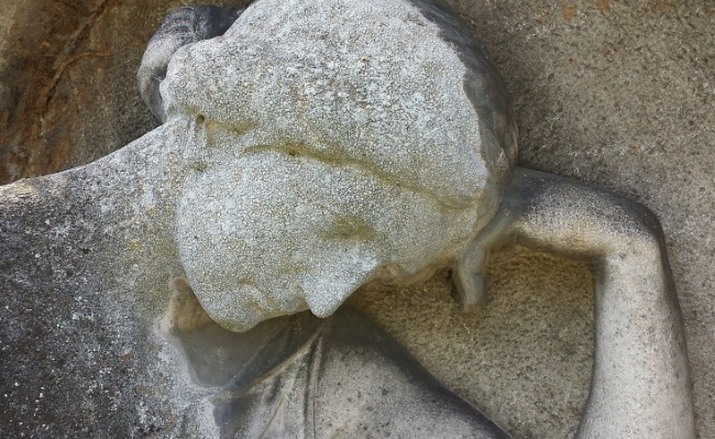 Kreikkalaistyyppistä naista esittävä vanha kivipatsas nojaa väsyneenä käteensä.